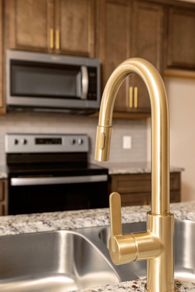 Elegant brass faucet in a modern kitchen setting with granite countertop and stainless steel appliances.