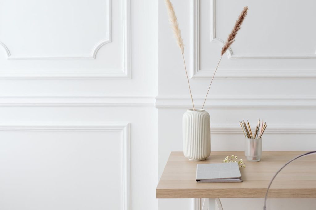 A minimalist home office setup with a wooden desk, notepad, and white vase.