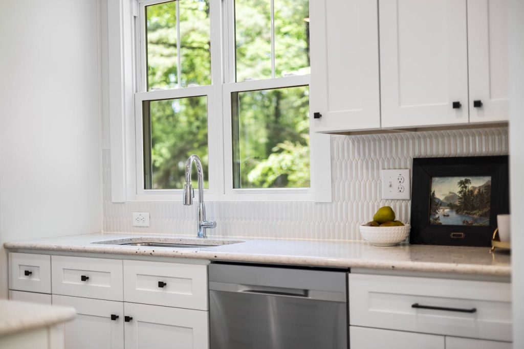 Contemporary white kitchen interior with natural light, featuring a sink and window view of greenery.